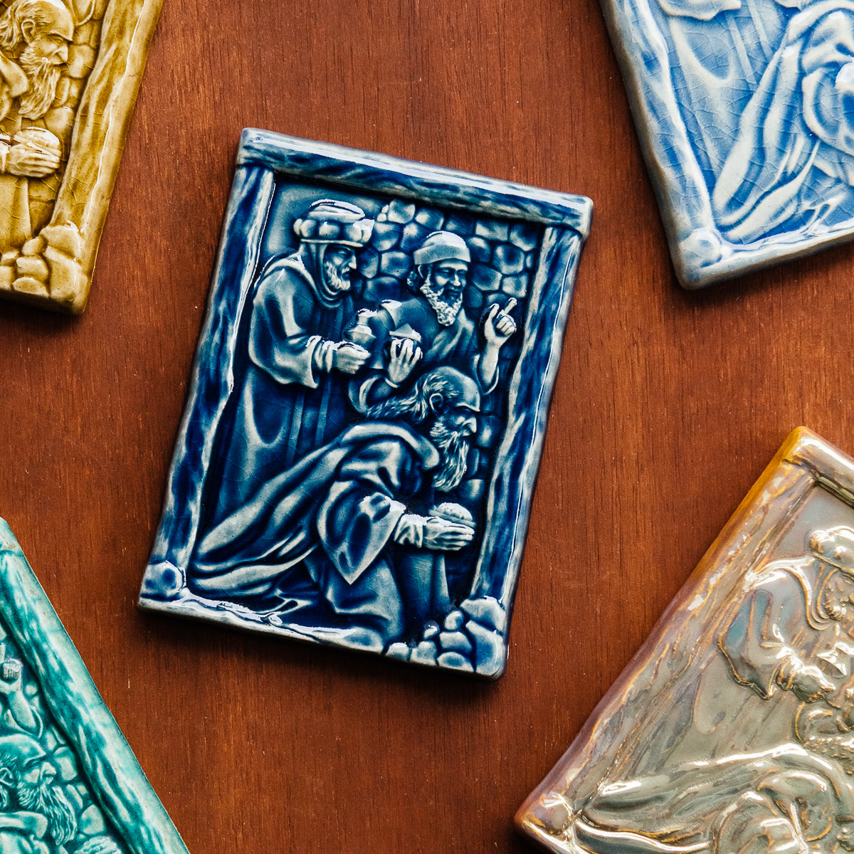 The Three Wise Men Tile features the wisemen in robes holding their three gifts- gold, frankincense and myrrh. They are all facing the right, they seem to be focused on one point. There is a stone wall behind them.