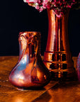 A set of Pewabic vases sit together on a wooden table. They all have the Copper Iridescent glaze.