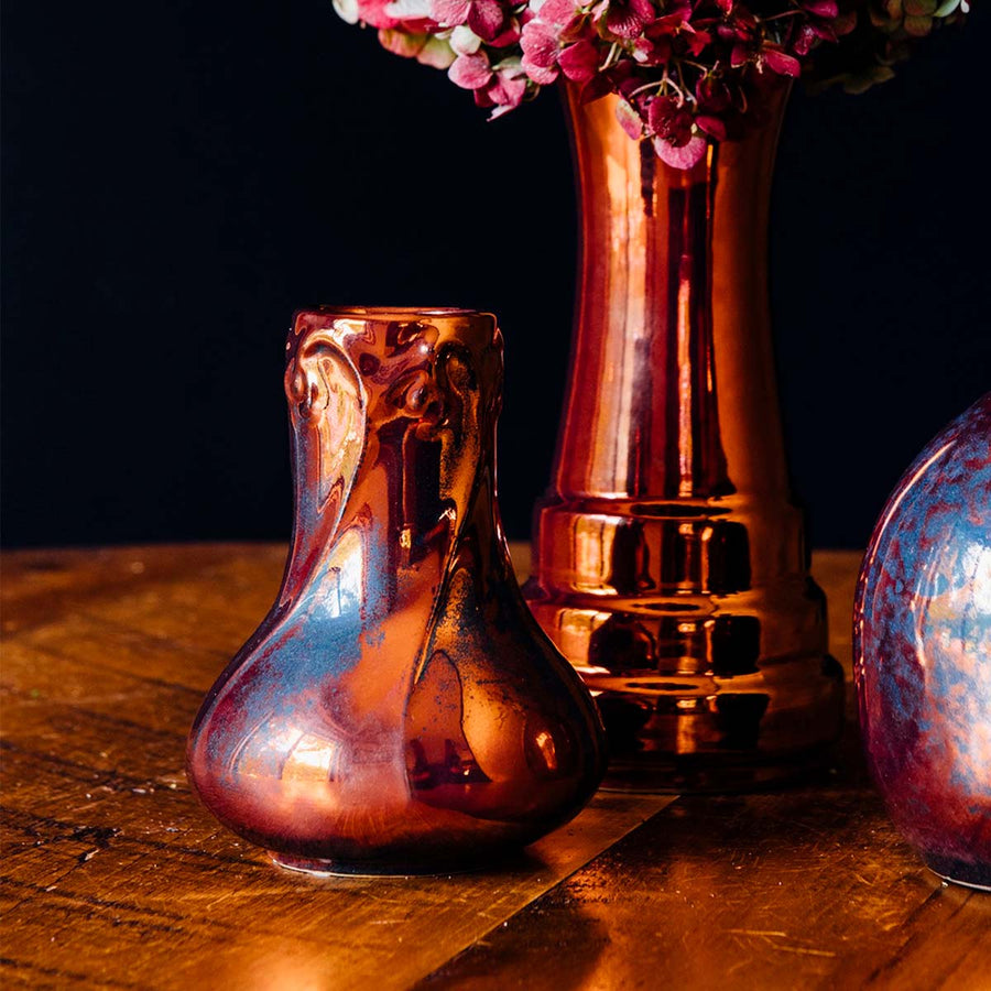 A set of Pewabic vases sit together on a wooden table. They all have the Copper Iridescent glaze.