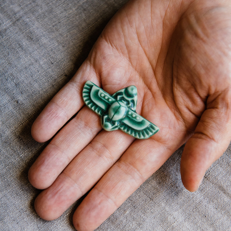 This high relief ceramic pin features a stylized scarab beetle with outstretched wings. The Scarab Pin featured is in our serene jewel-toned green “Pewabic Green” glaze. 