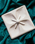 Geo Flower Tile in a snow white Alabaster glaze nestled in a rich, green velvet fabric.