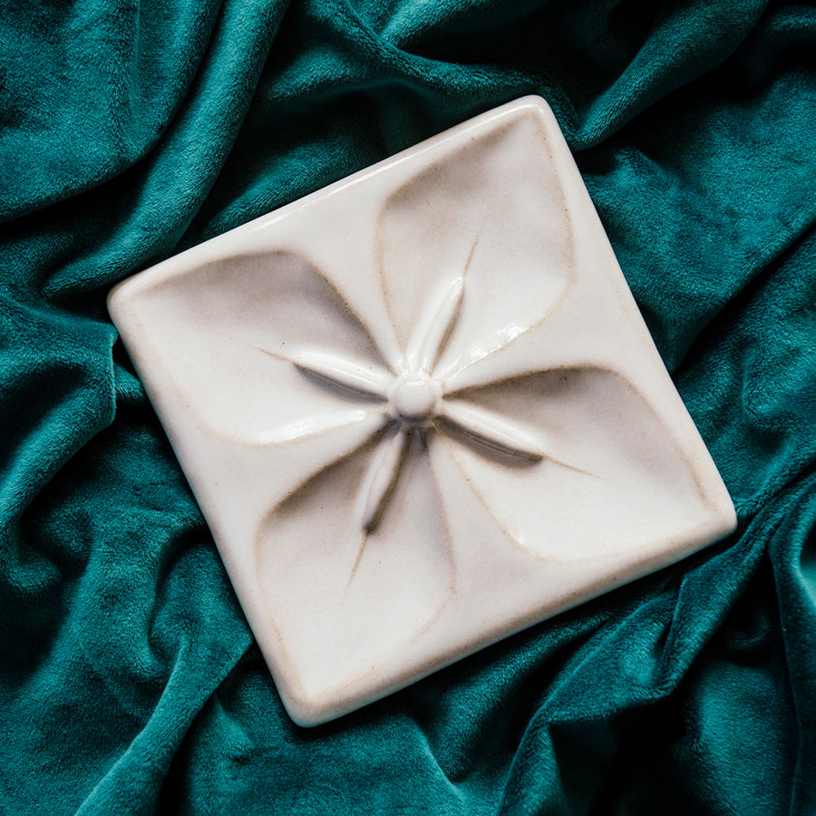 Geo Flower Tile in a snow white Alabaster glaze nestled in a rich, green velvet fabric.