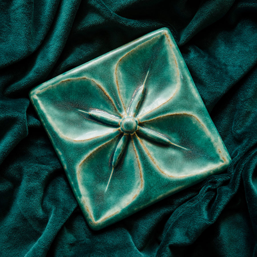 Geo Flower Tile in our classic Pewabic Blue glaze nestled in a rich, green velvet fabric.