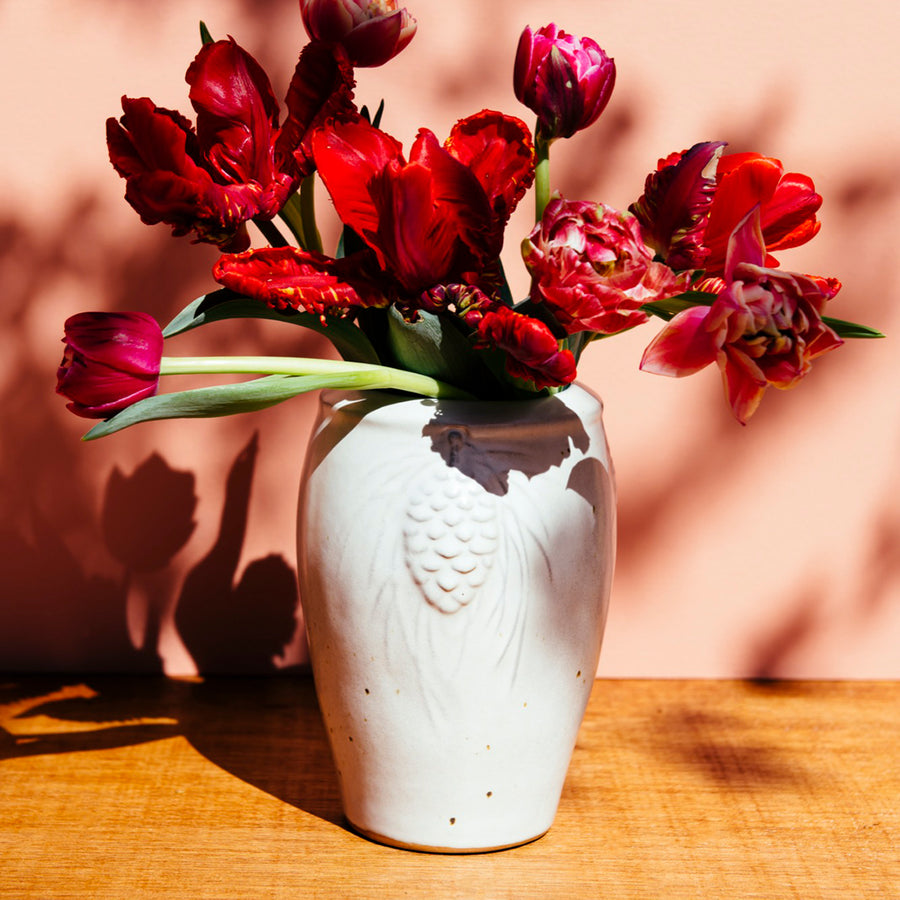 The Pinecone vase features smooth sides with three high relief pinecones and pine needles near the lip of the vessel. Each pinecone points in a different direction so there is always one pinecone pointed outword no matter which direction the vase is sitting. The top of the vase has a simple raised lip that come in toward the center.