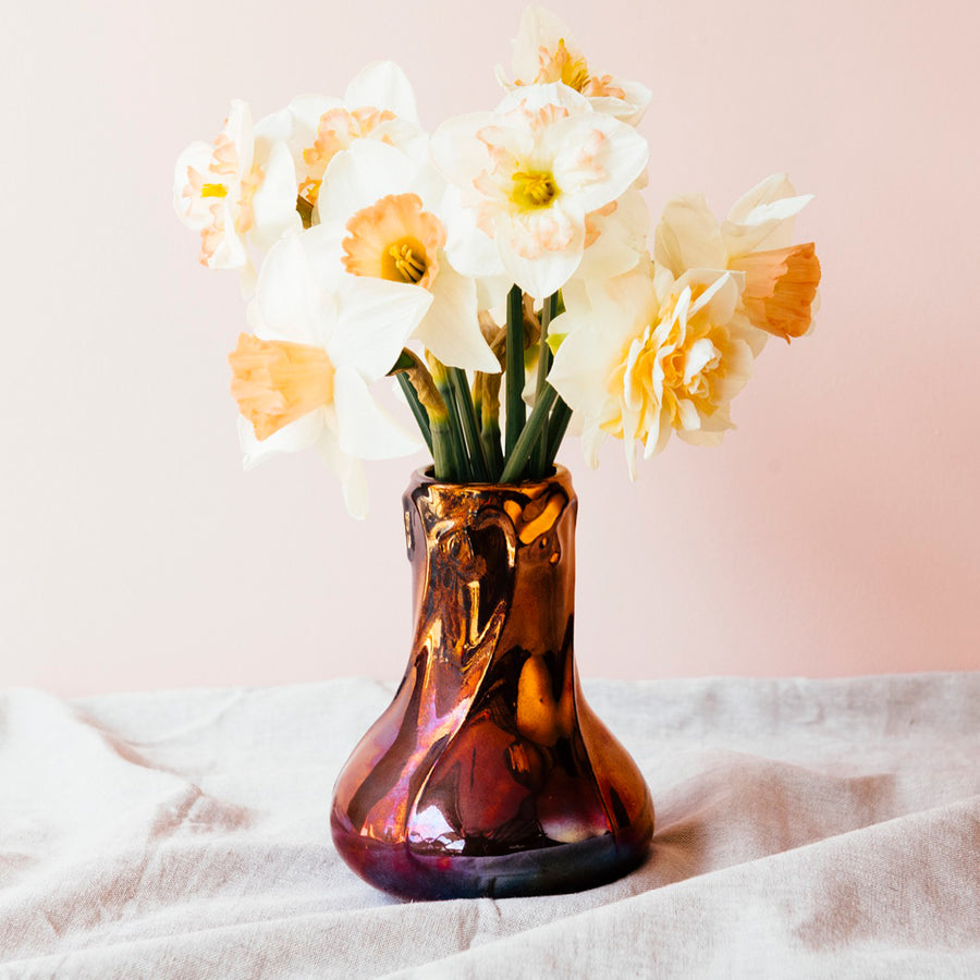 The Snowdrop vase has a wide, round base that contracts into a pillar as it gets taller. The rim of the vase has small snowdrop flowers whose stems glide gracefully down the sides of the vase.