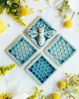 This Honey Bee Tile is featured in the medium blue Glacier Gloss glaze. It is set on a table surrounded by three honeycomb tiles in the same glossy glaze.
