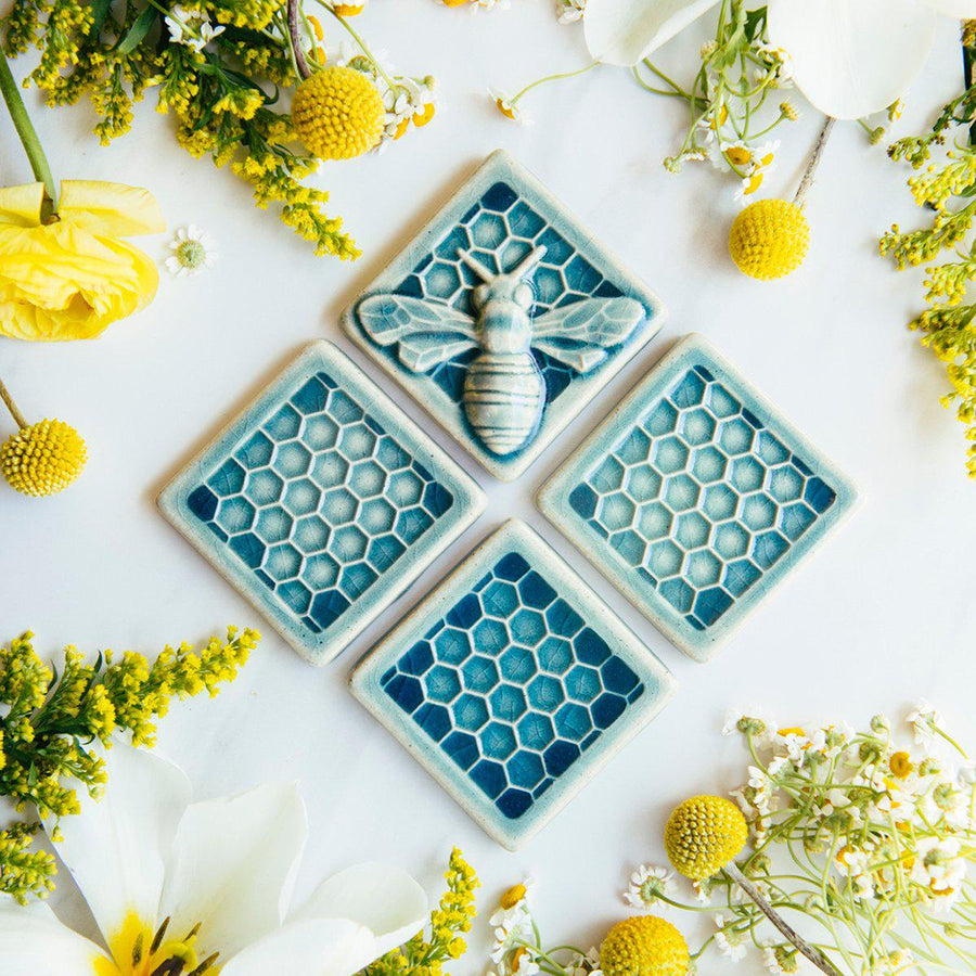 This Honey Bee Tile is featured in the medium blue Glacier Gloss glaze. It is set on a table surrounded by three honeycomb tiles in the same glossy glaze.