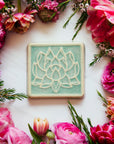 The Lotus tile features a line drawing of a blooming lotus flower, its pointed petals outstretching. It has a simple border around the design. This Lotus Tile features the glossy pale blue Celadon glaze.