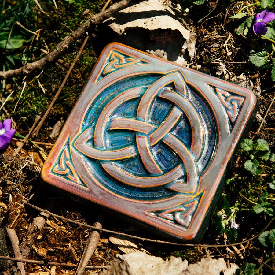 The Trinity Knot tile features a three-pointed Celtic knot interwoven with a circular ring. This knot is surrounded by a thick border with smaller three-pointed knots in each corner.