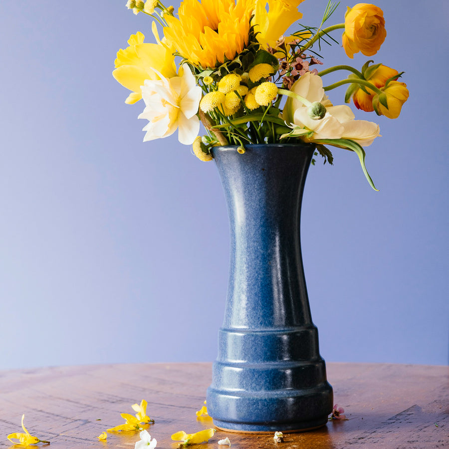 This vase is a sleek, slim vessel. At the base, there are three shallow "steps" with the widest at the bottom. The vase continues up in a smooth column that gets slightly wider at the top.