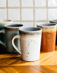 Five empty Cafe Mugs are set in a v pattern on a wooden countertop.