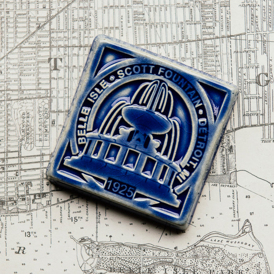 The ceramic Scott Fountain tile design features the Fountain itself in the center with the words "Belle Isle - Scott Fountain - Detroit, Michigan" around it. The date the tile was constructed - 1925 - is also featured at the bottom of the design. The tile is glazed in a glossy deep blue color.