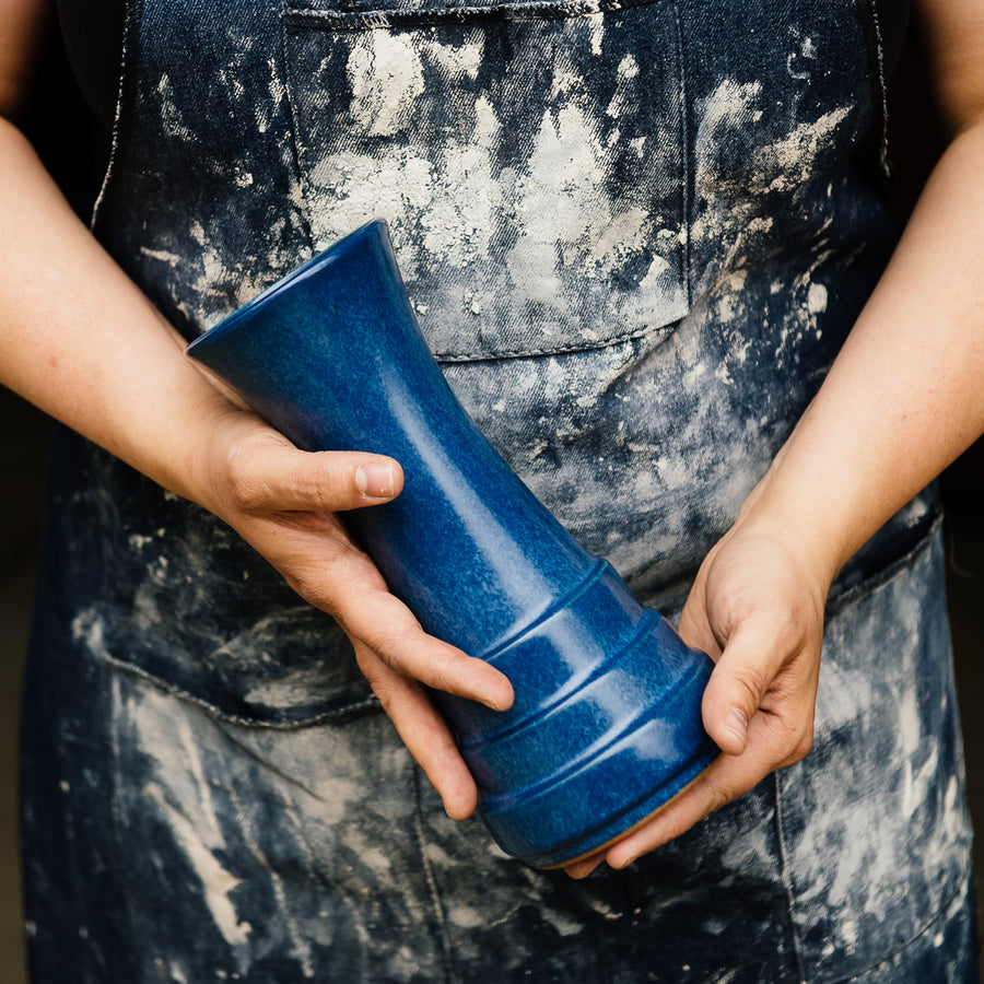 A Step Vase is held by a Pewabic artisan in a dusty denim apron.