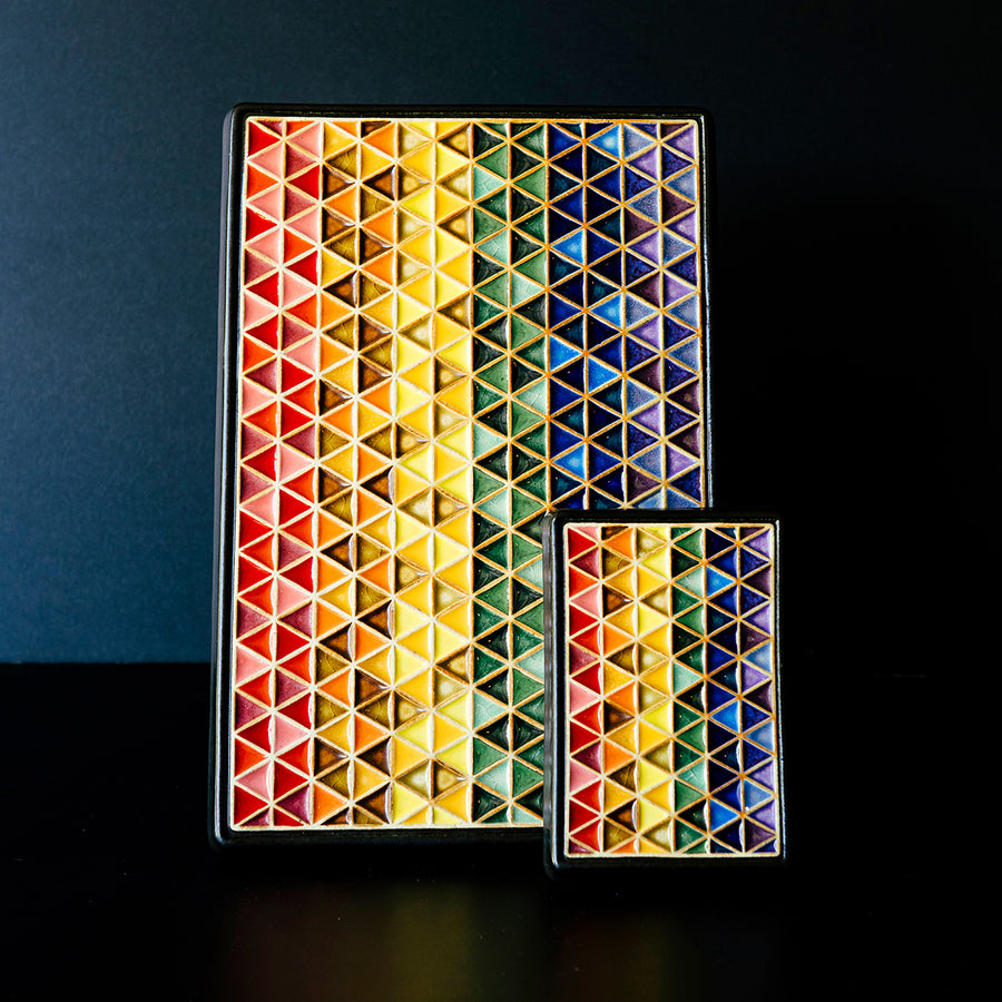 Both sizes of the Pride Tile sit next to each other. The much larger tile features more lines of interwoven triangles than the smaller version. But they have the same glaze colors and triangle pattern.