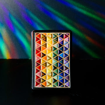 The 4x6 Pride Tile features lines of interlocking triangles, the colors on the triangles start at red and end in indigo- creating the rainbow Pride flag. The bright pattern is contained in a black border.
