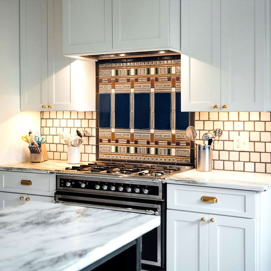 The detailed portions of the backsplash are contained behind the brushed silver stove with modern white cabinets.