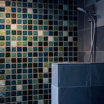 The moody blend of blues, greens, browns and whites are showcased on a large uninterrupted shower wall. The tiles are 3x3 square, all plain except for one which boasts the circular Pewabic logo.