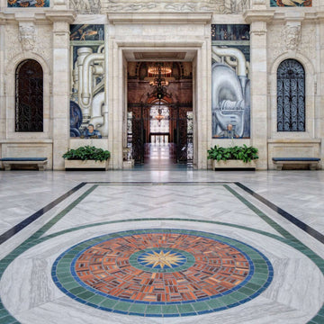 The Rivera Court boasts light intricately carves stone walls and larger-than-life murals, but we are focused on another art piece. The Pewabic tile floor mural features a circular mosaic pattern of blues, greens and rust colors. A star pattern bursts from the center with many points.