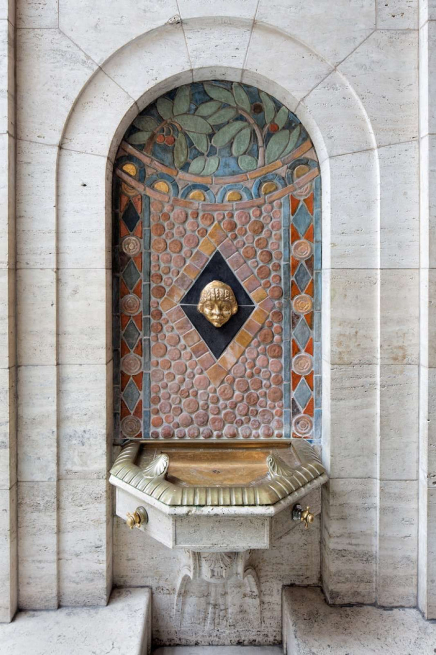 In the center of the drinking fountain is the golden head of a child in Aztec design. 