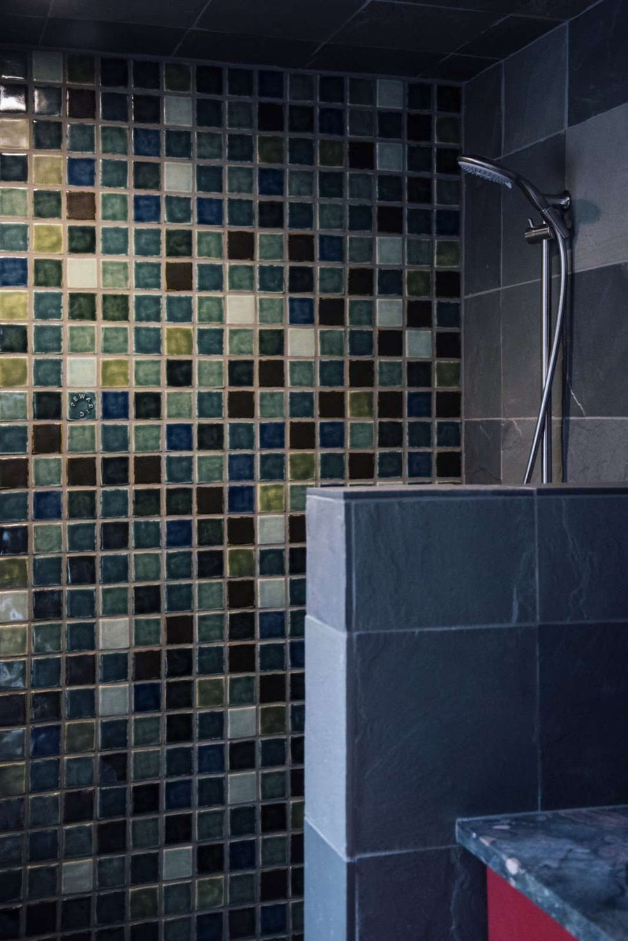 Further from the mosaic of color, there is a half wall with large dark gray marbled stone tile.