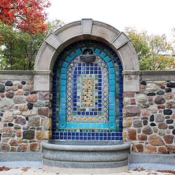 Square tiles in multiple shades of blue are positioned in different designs throughout this flat tile installation. It it tucked into an alcove on a stone wall.