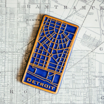 This rectangular Detroit Map Tile has a line drawing of the areal street view of downtown Detroit. The word "Detroit" is written at the bottom of the design.