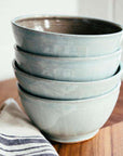 A stack of Frost glazed bowls sit on a wooden countertop.