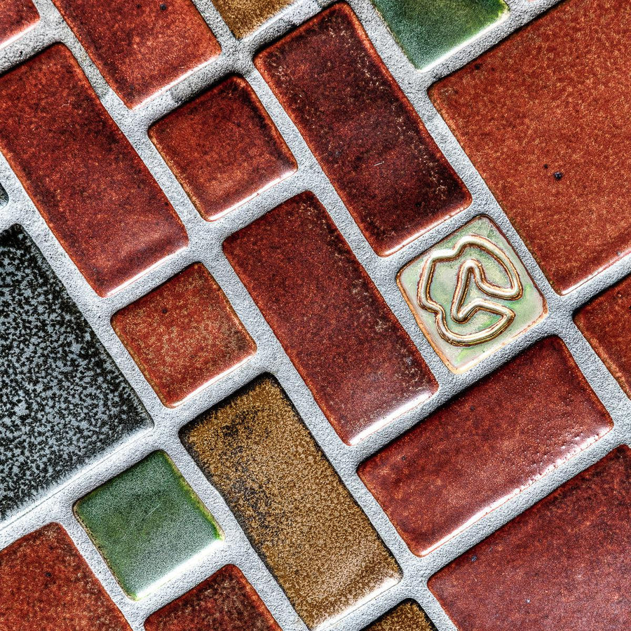 1:1 aspect ratio close-up shot of the red, tan, pine green, charcoal, and "blush" iridescent tiles in this autumnal design.