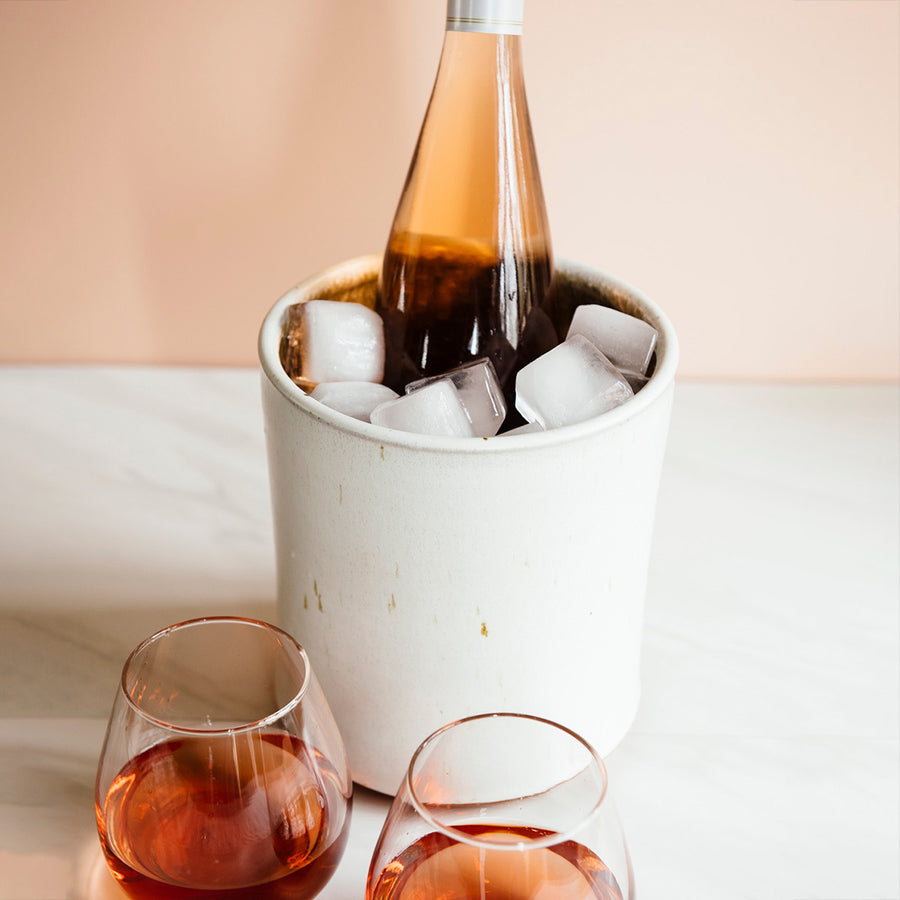 Another application of this functional vessel, this Crock is filled with ice and holds a bottle of rosé. Two stemless wine glasses hold more of the pale pink drink. 