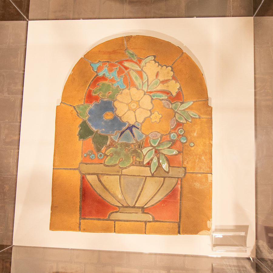 This flat tile installation features a pedestal bowl holding a large floral arrangement sitting in a window.