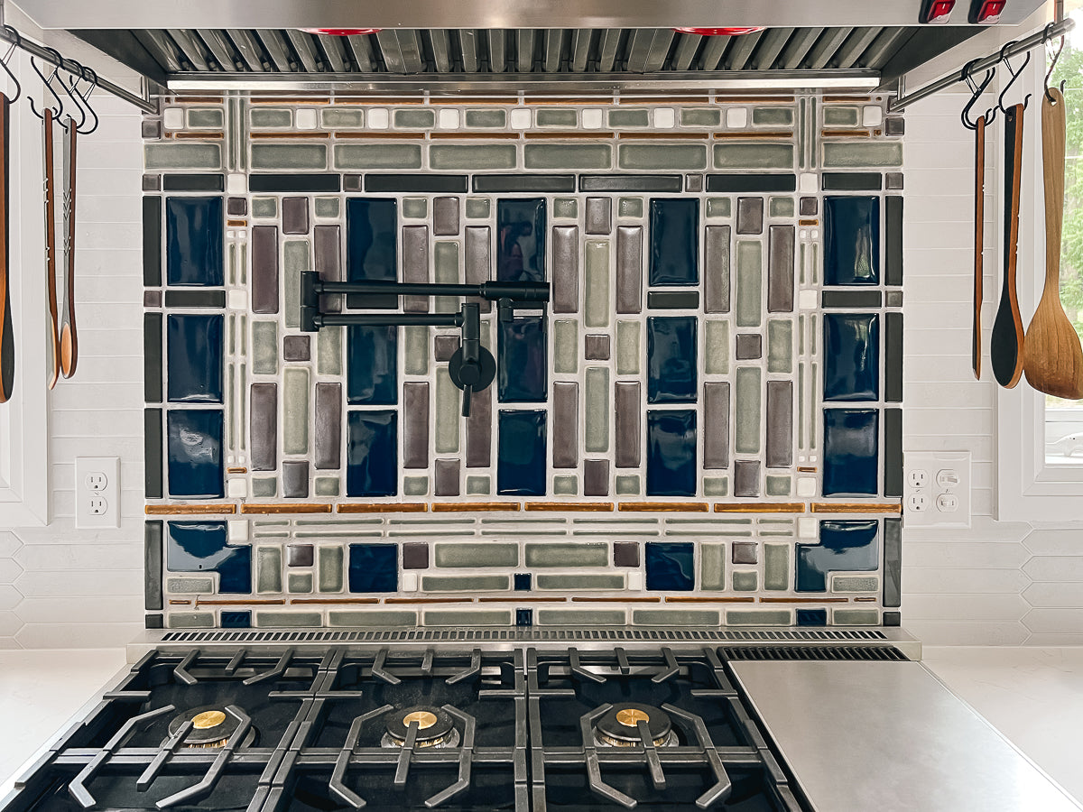 Straight on view of a custom kitchen backsplash prominently featuring glossy blue tiles alongside a blend of glossy grey tiles and matte finished tiles in an intricate geometric formation.