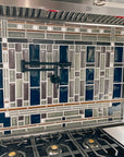 Side view of a custom kitchen backsplash prominently featuring glossy blue tiles alongside a blend of glossy grey tiles and matte finished tiles in an intricate geometric formation.