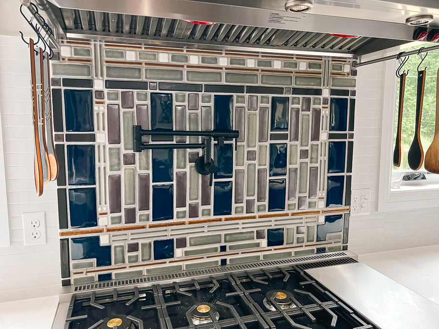 Side view of a custom kitchen backsplash prominently featuring glossy blue tiles alongside a blend of glossy grey tiles and matte finished tiles in an intricate geometric formation.