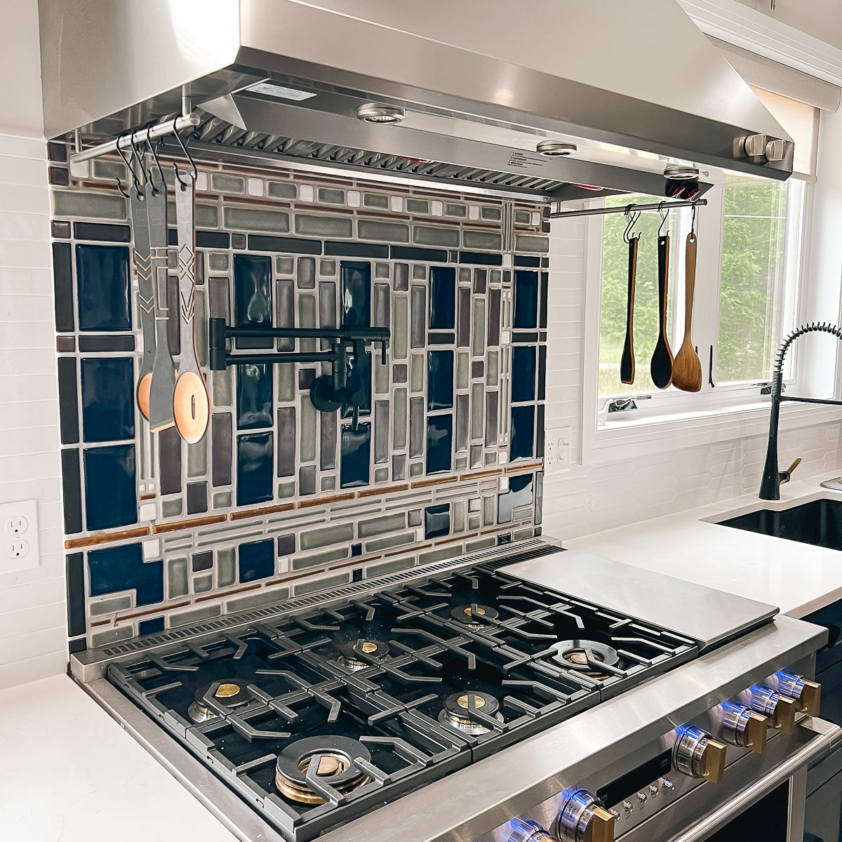 Side view of a custom kitchen backsplash prominently featuring glossy blue tiles alongside a blend of glossy grey tiles and matte finished tiles in an intricate geometric formation.