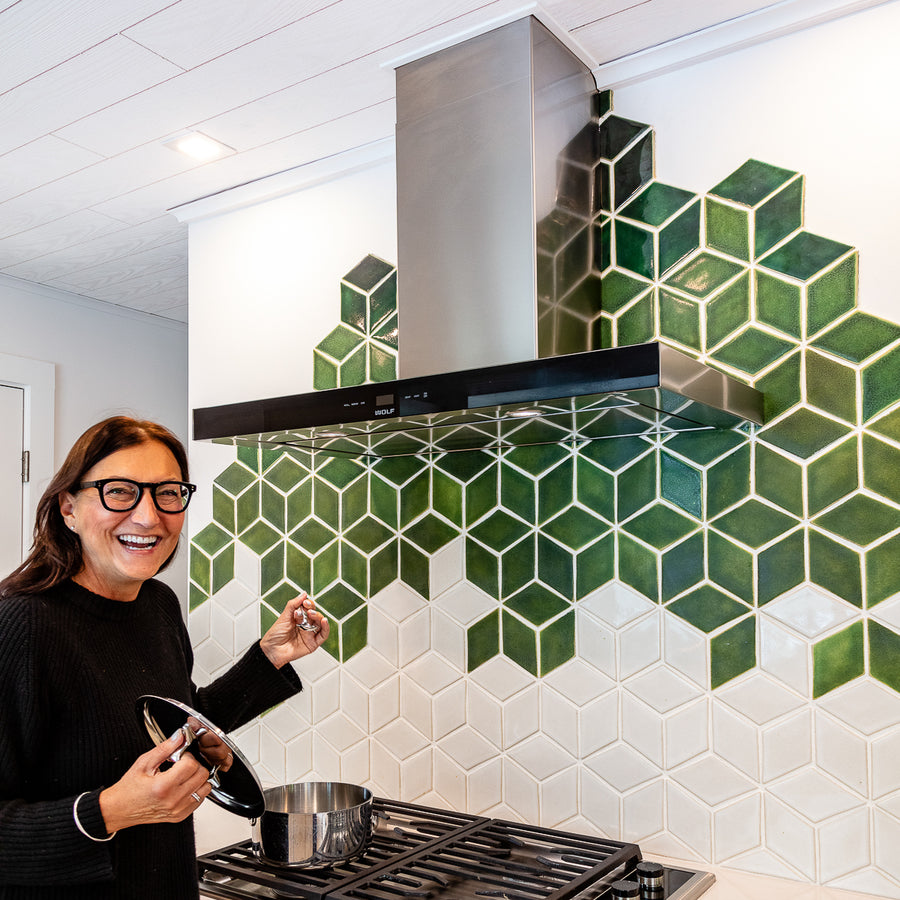 A quarter angle shot of the custom Green Rhombus Backsplash. There is a woman wearing glasses smiling as she opens the lid of a pot placed on the stove.