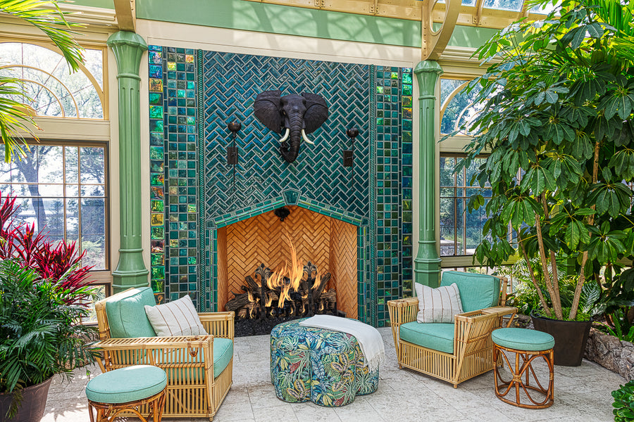 Horizontal, wide shot of the custom fireplace surrounded by topical plants, palms, and wicker furniture set.