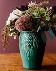 This Pinecone vase features the matte blueish-green Pewabic Green glaze, filled with a fall inspired flower arrangement featuring burgundy, rust, peach, and creme flowers.