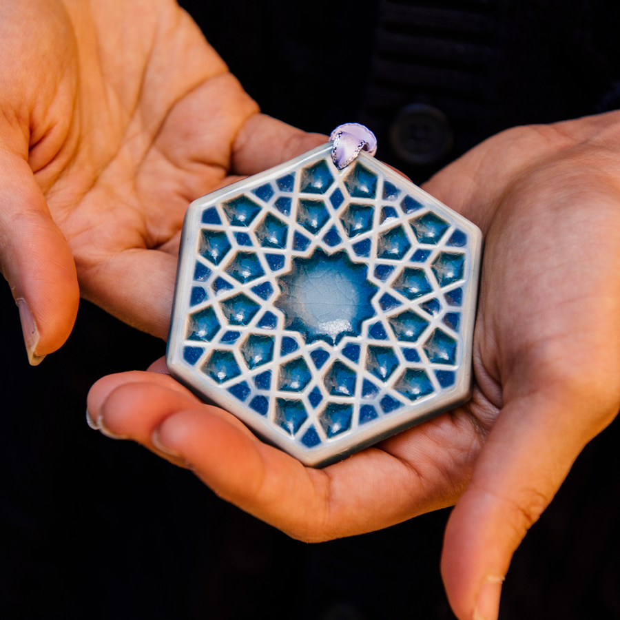 Our 2022 Snowflake Ornament named “Ice” in a high-gloss, light-blue, Glacier Gloss glaze held in two hands. The design is geometric and reminds one of stained glass. 