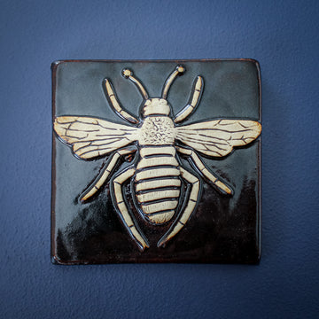 This black and cream tile features a detailed bee with arms and wings outstretched.