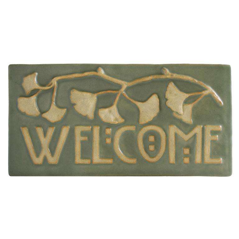 The Ginkgo Welcome Tile features the word "Welcome" in Arts and Crafts style font with a branch of ginkgo leaves above it. The leaves and wording are scraped giving them a creamy off-white color with a pale green glazed background.