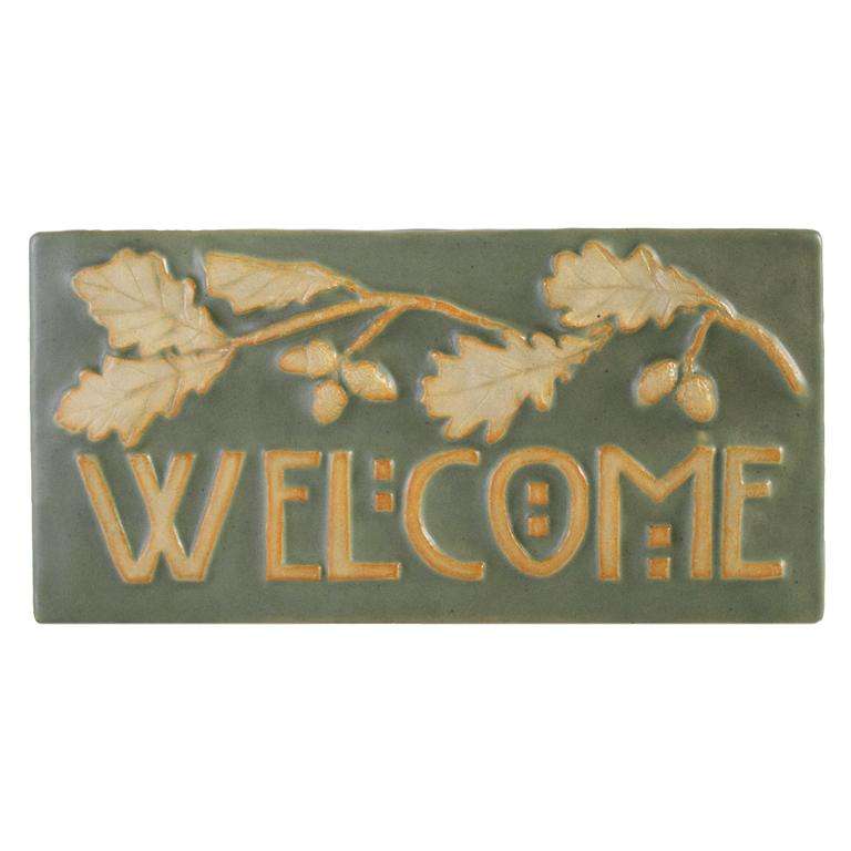 This Oak Welcome Tile features a long oak branch with leaves and acorns. Under the branch is the word "Welcome" in stylized Arts and Crafts style writing. The branch and words are scraped of glaze, giving them a creamy white color while the background is pale green.